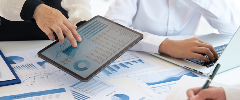 two men working with a tablet and various printed charts below, depicting fundamental analysis