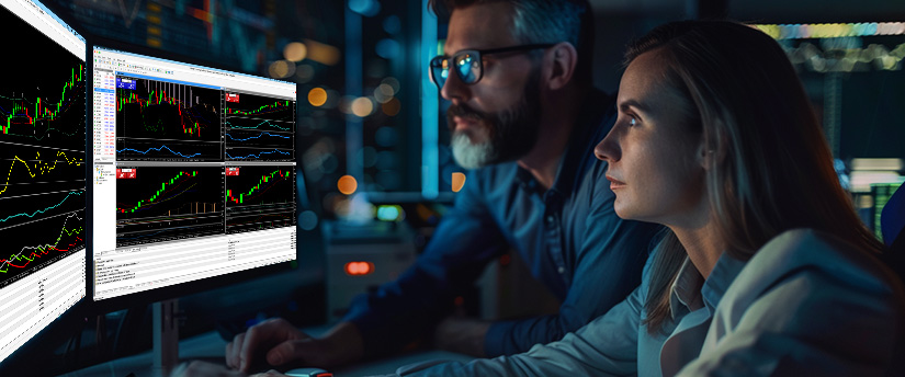A man and woman forex traders analyzing trading charts on computer screens, focused on forex trading psychology and how to stay calm during market volatility.