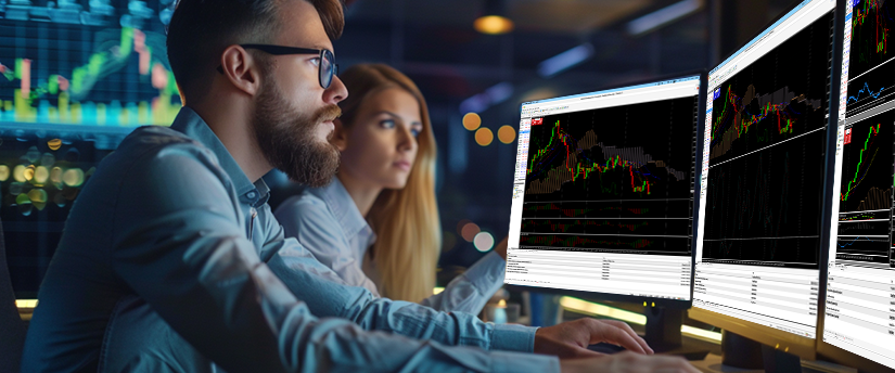 A man and a woman intently view multiple computer monitors displaying financial trading charts while learning how to use Expert Advisors in Forex.