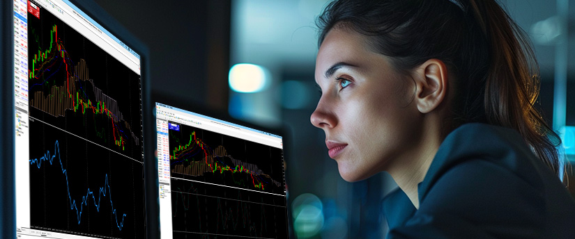 A focused woman analyzes financial charts on computer screens in a dimly lit room. The serious atmosphere highlights dedication and concentration while exploring what is trading income and evaluating market performance.